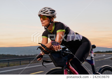 Female Cyclist Training on Road Bike at Sunset Wearing Helmet and Sunglasses for Endurance Female Cyclist Training on Road Bike at Sunset Wearing Helmet and Sunglasses for Endurance 142919870