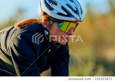 Focused Female Cyclist Wearing Helmet And Reflective Sunglasses During Outdoor Training Ride At Sunrise Focused Female Cyclist Wearing Helmet And Reflective Sunglasses During Outdoor Training Ride At Sunrise 142919872