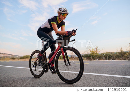 Female Cyclist Training on Road Bike at Sunset in Aerodynamic Position for Speed and Endurance Female Cyclist Training on Road Bike at Sunset in Aerodynamic Position for Speed and Endurance 142919901