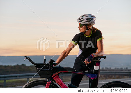 Female Cyclist Training on Road Bike at Sunset Preparing for Triathlon Race Female Cyclist Training on Road Bike at Sunset Preparing for Triathlon Race 142919911