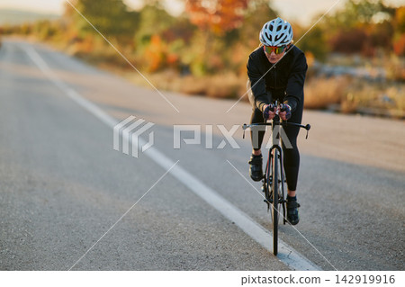 Female Cyclist Training on Open Road During Autumn Sunrise Workout Female Cyclist Training on Open Road During Autumn Sunrise Workout 142919916