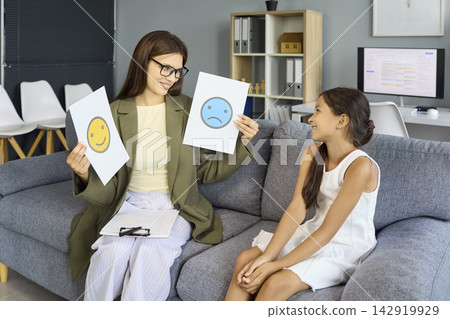 Child therapist showing happy and sad emotion cards to girl during counseling Child therapist showing happy and sad emotion cards to girl during counseling 142919929