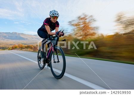Female Cyclist Riding a High-Speed Road Bike Through Scenic Autumn Countryside Female Cyclist Riding a High-Speed Road Bike Through Scenic Autumn Countryside 142919930