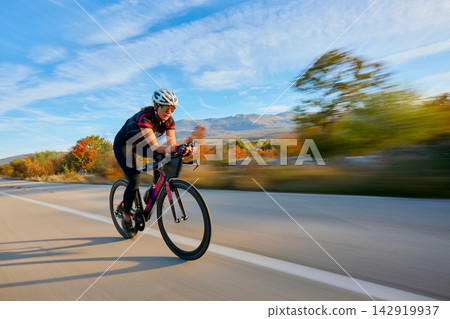 Female Cyclist Riding Fast on Road Bike Through Scenic Countryside During Autumn Training Ride Female Cyclist Riding Fast on Road Bike Through Scenic Countryside During Autumn Training Ride 142919937