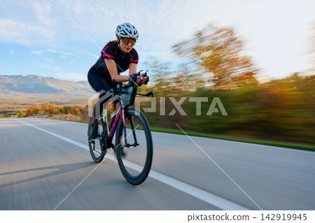 Female Cyclist Road Cycling at Speed on Open Road With Autumn Landscape and Mountains Female Cyclist Road Cycling at Speed on Open Road With Autumn Landscape and Mountains 142919945