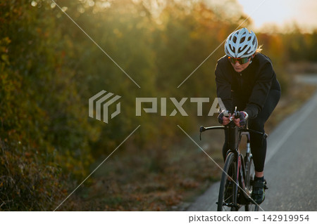 Female Road Cyclist Training on Quiet Country Road at Sunset With Aero Bike and Helmet Female Road Cyclist Training on Quiet Country Road at Sunset With Aero Bike and Helmet 142919954