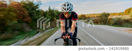 Female Cyclist Training on Open Road, Speeding Through Autumn Countryside at Sunset Female Cyclist Training on Open Road, Speeding Through Autumn Countryside at Sunset 142919980