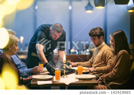 Family Dinner in Restaurant With Waiter Serving Food at Candlelit Table During Evening Out Family Dinner in Restaurant With Waiter Serving Food at Candlelit Table During Evening Out 142919985