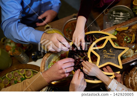 Family Reaching for Dates Around Ramadan Mubarak Star Bowl During Festive Iftar Gathering Family Reaching for Dates Around Ramadan Mubarak Star Bowl During Festive Iftar Gathering 142920005