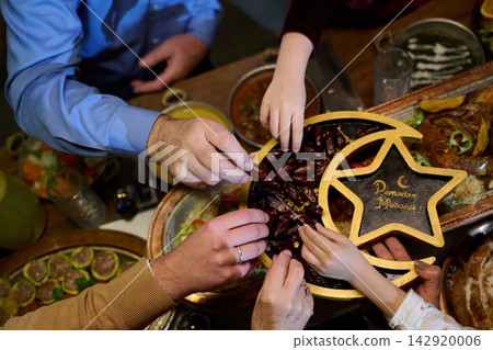 Ramadan Family Sharing Dates At Iftar Table Celebrating Ramadan Mubarak With Hands Reaching For Fruit 142920006