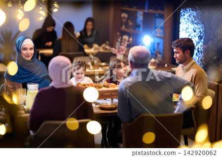 Multigenerational Family Dinner In Restaurant With Woman Wearing Hijab And Children Sharing Food Multigenerational Family Dinner In Restaurant With Woman Wearing Hijab And Children Sharing Food 142920062