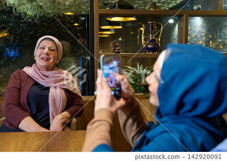 Grandmother Posing While Granddaughter Takes Photo In Cozy Cafe With Decorative Teapots Grandmother Posing While Granddaughter Takes Photo In Cozy Cafe With Decorative Teapots 142920091