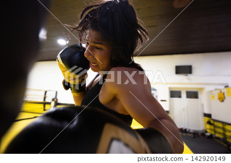 Female Boxer Training in Gym Throwing Powerful Punch in Intense Close-Up Action Shot Female Boxer Training in Gym Throwing Powerful Punch in Intense Close-Up Action Shot 142920149