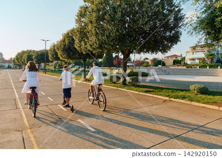 Family Cycling And Scootering Together On Seaside Promenade During Golden Hour 142920150