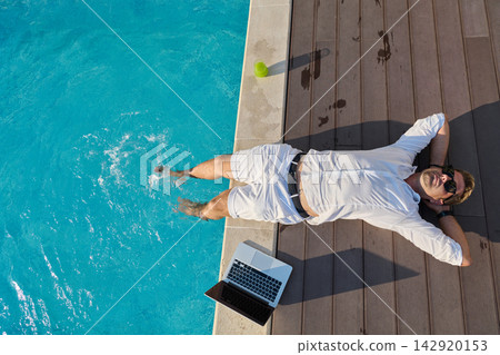 Relaxed Man in White Outfit With Laptop Cooling Feet in Poolside on Sunny Summer Morning 142920153