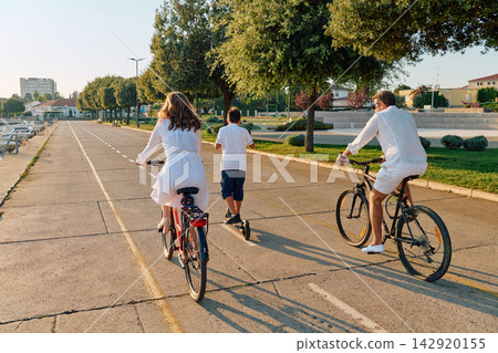 Family Riding Bikes and Scooter Along Coastal Promenade at Sunset 142920155