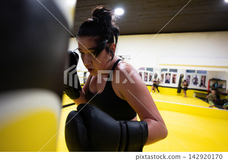 Determined Female Boxer Training With Punching Bag in Yellow Boxing Gym During Intense Workout Session Determined Female Boxer Training With Punching Bag in Yellow Boxing Gym During Intense Workout Session 142920170