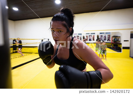 Determined Female Boxer Training in Yellow Gym Ring Wearing Gloves and Intense Focus Determined Female Boxer Training in Yellow Gym Ring Wearing Gloves and Intense Focus 142920172