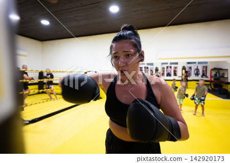 Determined Female Boxer Training With Gloves in Bright Yellow Gym Ring During Intense Workout Determined Female Boxer Training With Gloves in Bright Yellow Gym Ring During Intense Workout 142920173
