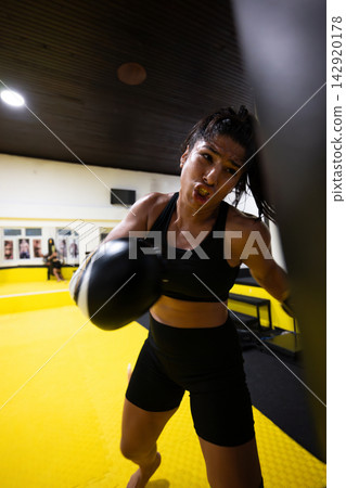 Determined Female Boxer Training Intense Workout Punching Bag In Gym With Focused Expression Determined Female Boxer Training Intense Workout Punching Bag In Gym With Focused Expression 142920178