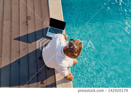 Man Working Remotely By a Pool With Laptop on Deck During Sunny Summer Morning Man Working Remotely By a Pool With Laptop on Deck During Sunny Summer Morning 142920179