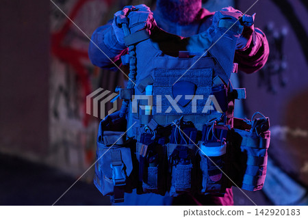 Tactical Plate Carrier Vest With Pouches and Gear Held by Operator in Urban Night Lighting Tactical Plate Carrier Vest With Pouches and Gear Held by Operator in Urban Night Lighting 142920183