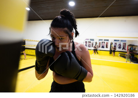 Determined Female Boxer Training in Yellow Gym Ring With Gloves During Intense Workout Session Determined Female Boxer Training in Yellow Gym Ring With Gloves During Intense Workout Session 142920186
