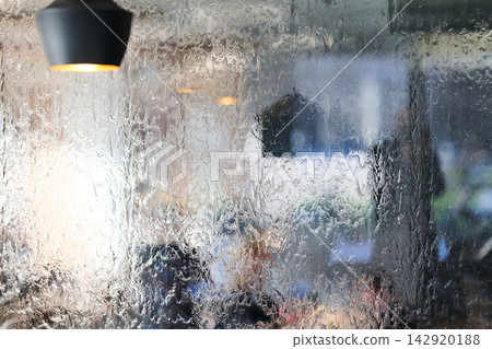 Rain-Soaked Window Overlooking Blurred Cafe Interior With Warm Pendant Lamp And People Rain-Soaked Window Overlooking Blurred Cafe Interior With Warm Pendant Lamp And People 142920188