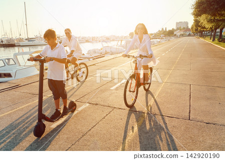 Family Riding Bikes and Scooter Along Marina Promenade at Sunset Parents and Son Enjoying Summer Family Riding Bikes and Scooter Along Marina Promenade at Sunset Parents and Son Enjoying Summer 142920190