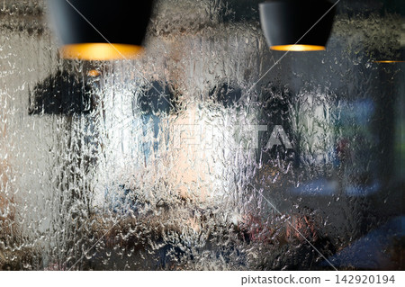 Wet Window With Blurred Cafe Interior and Hanging Lamps Through Rain Soaked Glass Wet Window With Blurred Cafe Interior and Hanging Lamps Through Rain Soaked Glass 142920194