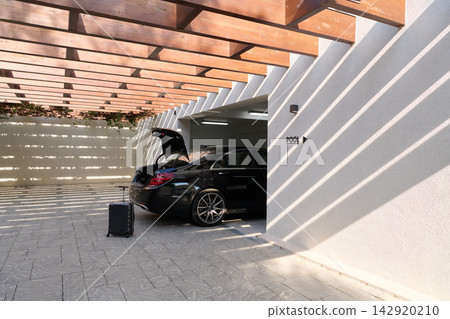 Luxury Sedan With Open Trunk and Luggage Parked in Modern Garage Near Pool at Sunny Resort 142920210