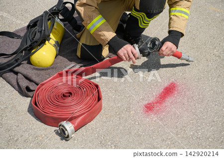 Firefighter Kneeling Connecting Red Fire Hose to Nozzle Beside Air Tank During Drill Firefighter Kneeling Connecting Red Fire Hose to Nozzle Beside Air Tank During Drill 142920214
