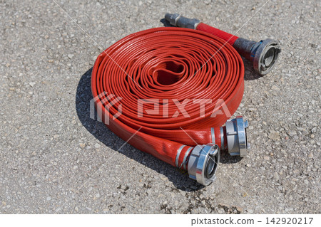 Rolled Red Fire Hose With Metal Couplings On Pavement Ready For Firefighting Use Rolled Red Fire Hose With Metal Couplings On Pavement Ready For Firefighting Use 142920217