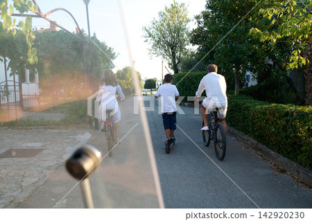 Family Biking and Scootering Together on a Quiet Residential Street During Summer Vacation Family Biking and Scootering Together on a Quiet Residential Street During Summer Vacation 142920230