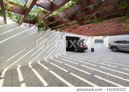 Modern Covered Garage With Luxury Cars, Pergola Shadows, Open Trunk and Luggage on Stone Driveway Modern Covered Garage With Luxury Cars, Pergola Shadows, Open Trunk and Luggage on Stone Driveway 142920322