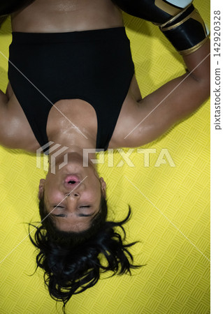 Exhausted Female Boxer Lying on Yellow Mat After Intense Workout, Catching Her Breath Exhausted Female Boxer Lying on Yellow Mat After Intense Workout, Catching Her Breath 142920328