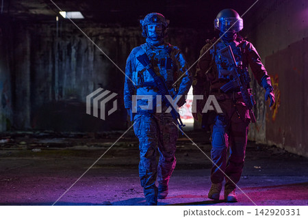 Two Tactical Soldiers Walking With Rifles in Dim Urban Abandoned Building With Colored Lighting Two Tactical Soldiers Walking With Rifles in Dim Urban Abandoned Building With Colored Lighting 142920331