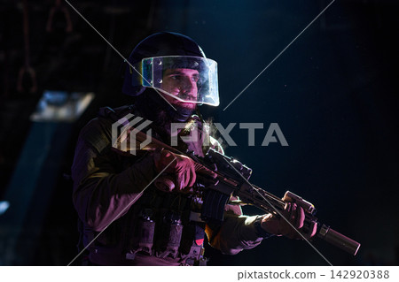 Armed Tactical Operator in Riot Helmet and Ballistic Visor Holding Rifle in Low-Light Environment Armed Tactical Operator in Riot Helmet and Ballistic Visor Holding Rifle in Low-Light Environment 142920388