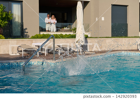 Couple Watching Pool Splash From Balcony At Modern Luxury Home During Summer Vacation Couple Watching Pool Splash From Balcony At Modern Luxury Home During Summer Vacation 142920393