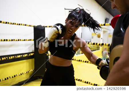 Female Boxer Training Aggressively in Yellow Boxing Ring During Intense Sparring Session With Coach Female Boxer Training Aggressively in Yellow Boxing Ring During Intense Sparring Session With Coach 142920396