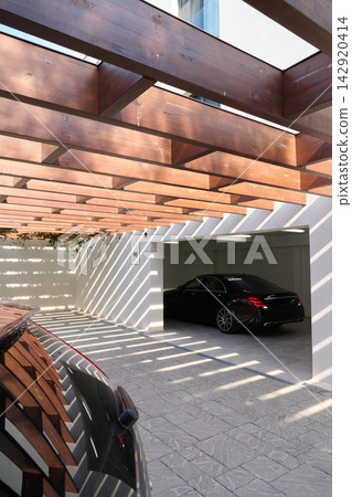 Modern Luxury Garage With Black Car Under Wooden Pergola Casting Dramatic Shadows Over Driveway Modern Luxury Garage With Black Car Under Wooden Pergola Casting Dramatic Shadows Over Driveway 142920414