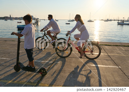 Family Cycling and Scooter Ride Along Seaside Promenade at Sunset by Marina 142920467
