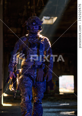 Armed Soldier In Tactical Gear Walking Through Dimly Lit Urban Ruins With Sunbeam Backlight Armed Soldier In Tactical Gear Walking Through Dimly Lit Urban Ruins With Sunbeam Backlight 142920476