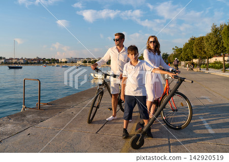 Family Biking on Waterfront Promenade in Umag Parents and Son With Bicycles and E Scooter Family Biking on Waterfront Promenade in Umag Parents and Son With Bicycles and E Scooter 142920519