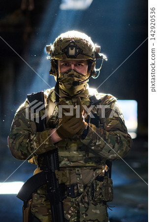 Camouflaged Soldier In Tactical Gear With Rifle Standing In Dramatic Light Camouflaged Soldier In Tactical Gear With Rifle Standing In Dramatic Light 142920536