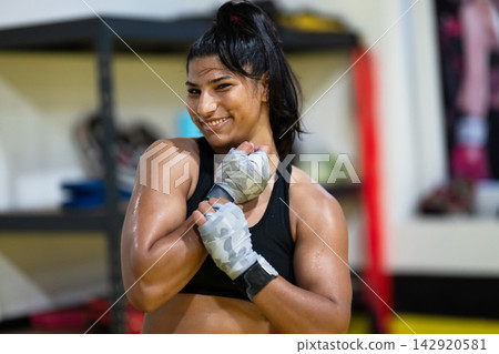Confident Female Boxer Training in Gym With Hand Wraps and Smiling After Workout Confident Female Boxer Training in Gym With Hand Wraps and Smiling After Workout 142920581