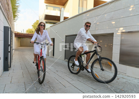 Happy Couple Riding Bicycles Together Near Modern Villa During Sunny Morning Leisure Vacation 142920593