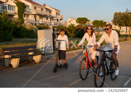 Family Riding Bikes and Electric Scooter Along Coastal Promenade in Umag at Sunset Family Riding Bikes and Electric Scooter Along Coastal Promenade in Umag at Sunset 142920697