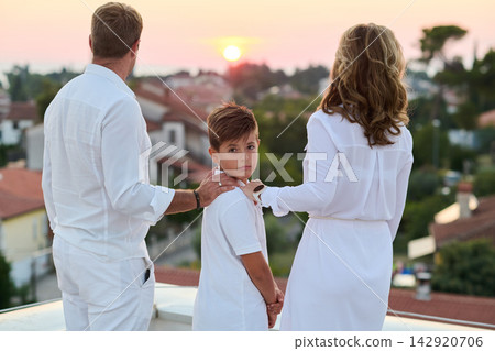 Family on Balcony at Sunset Overlooking Town and Sea Parents and Child on Rooftop Terrace Family on Balcony at Sunset Overlooking Town and Sea Parents and Child on Rooftop Terrace 142920706