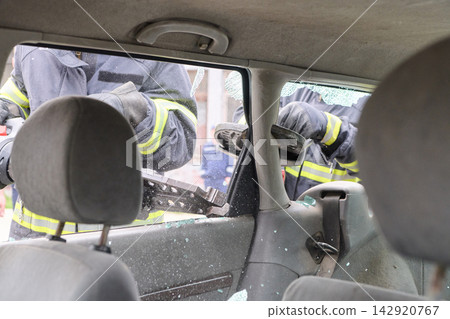 Firefighters Using Hydraulic Rescue Tool to Break Car Window During Emergency Vehicle Extrication Training Firefighters Using Hydraulic Rescue Tool to Break Car Window During Emergency Vehicle Extrication Training 142920767